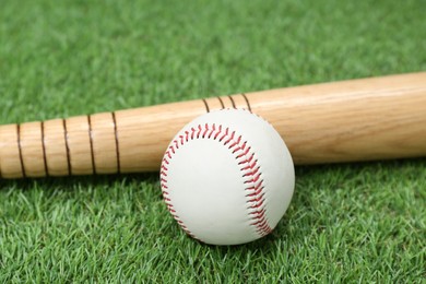 Photo of Wooden baseball bat and ball on green grass, closeup. Sports equipment