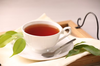 Aromatic tea in cup, saucer, spoon and green leaves on table