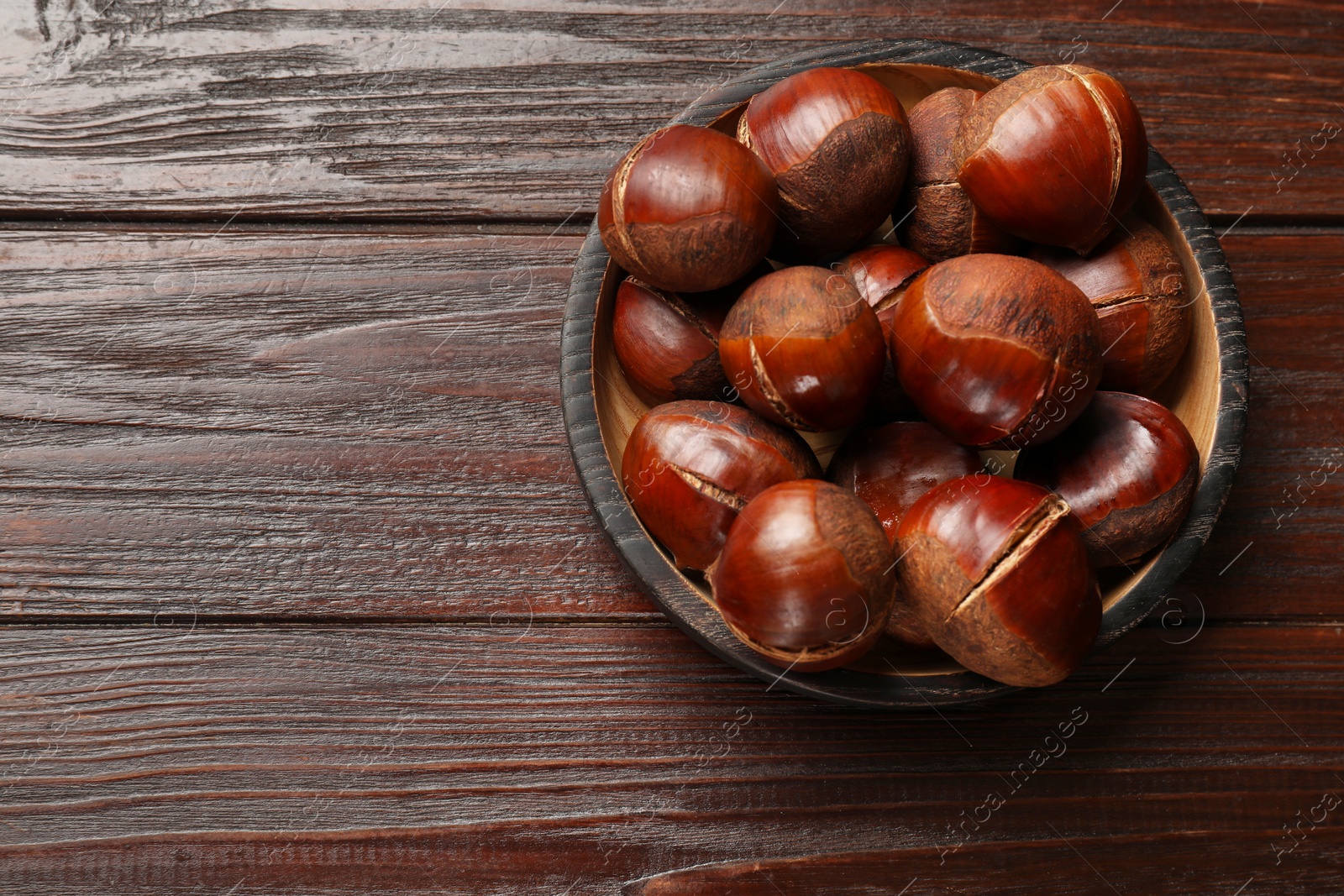 Photo of Roasted edible sweet chestnuts on wooden table, top view. Space for text