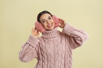 Photo of Beautiful young woman wearing earmuffs on beige background