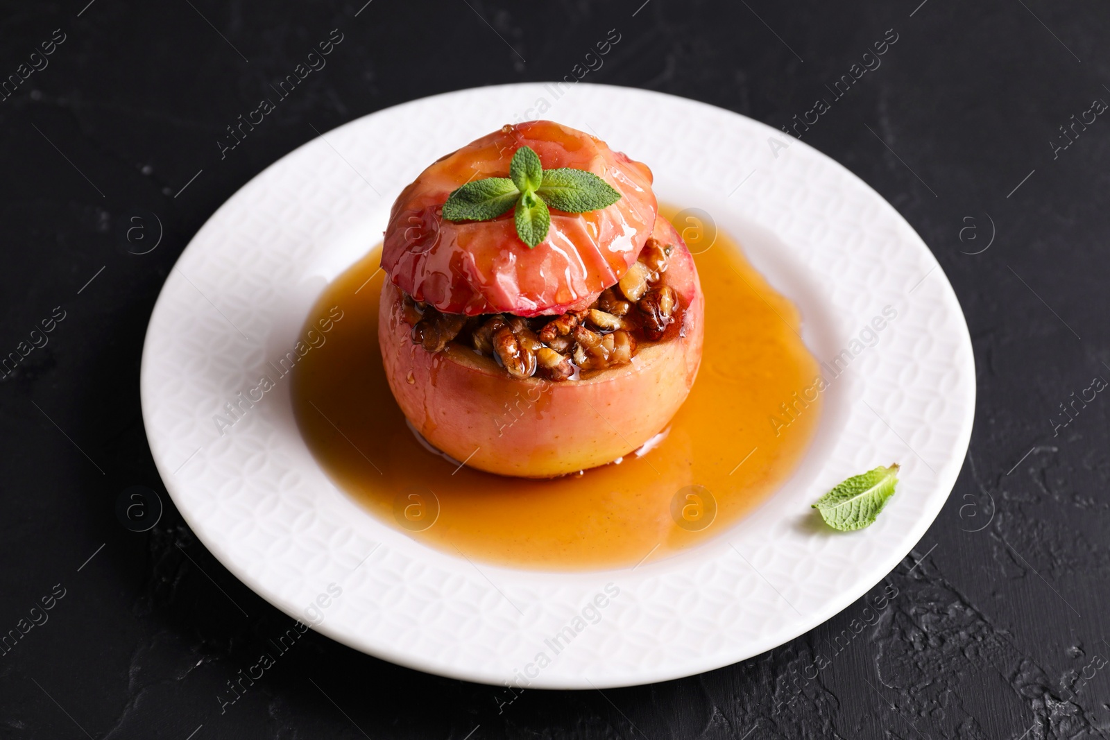 Photo of Tasty baked apple with nuts, honey and mint on gray textured table