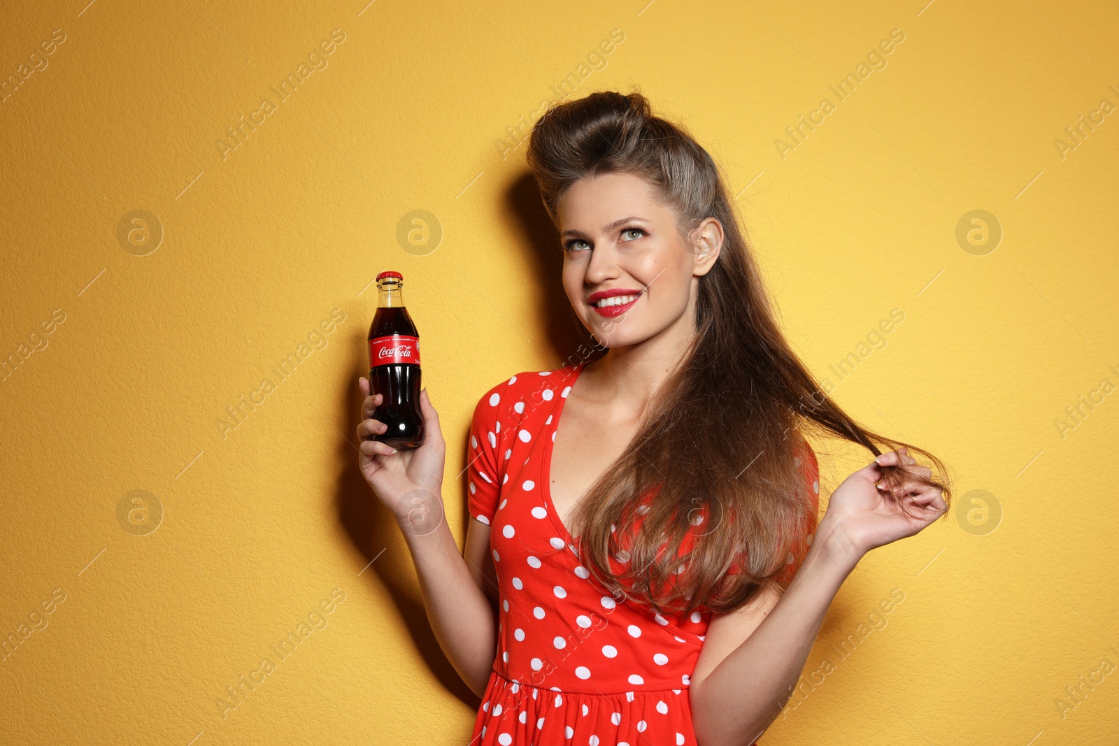 Photo of MYKOLAIV, UKRAINE - NOVEMBER 28, 2018: Young woman with bottle of Coca-Cola on color background