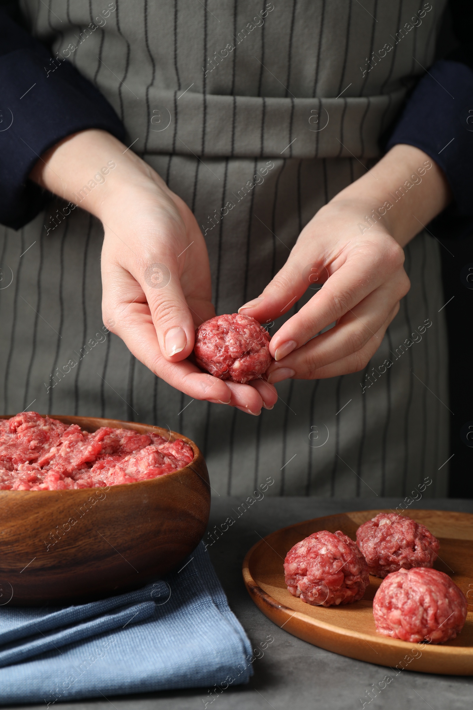 Photo of Woman making meatball from ground meat at grey table, closeup