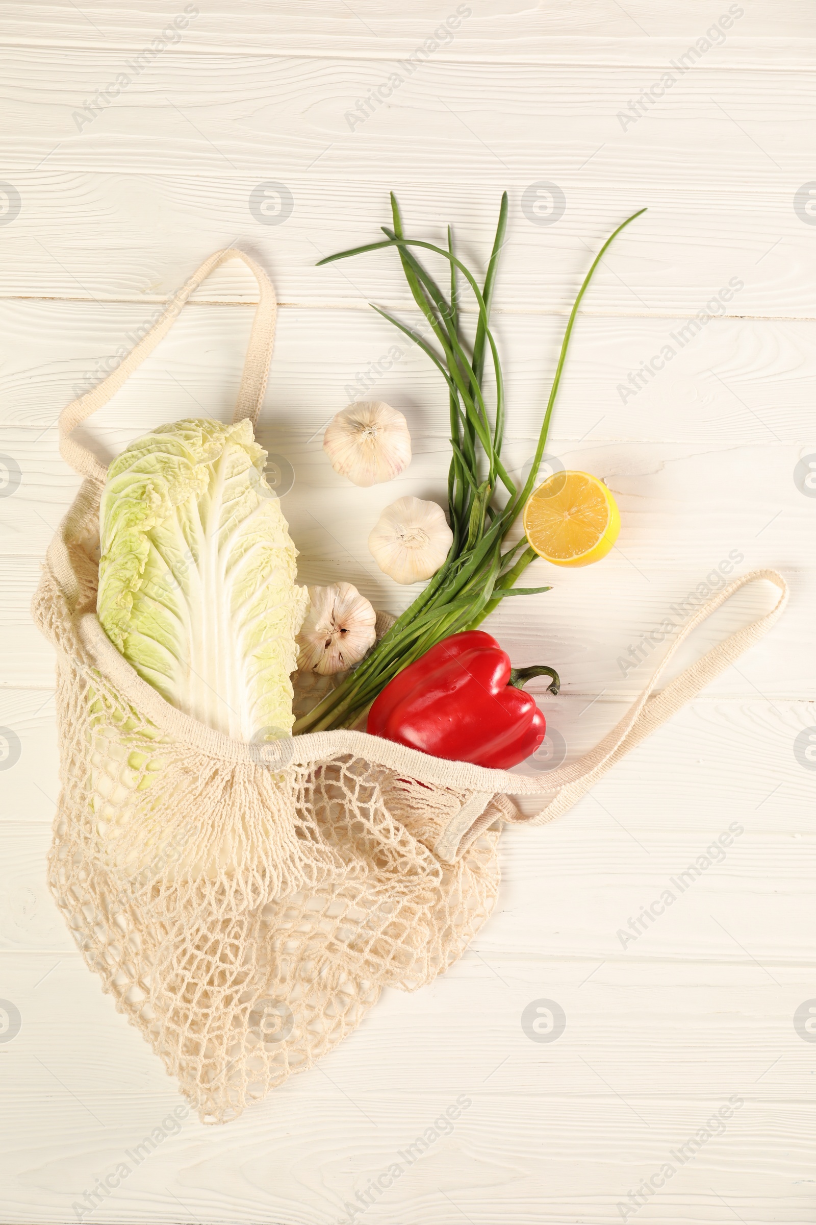 Photo of Fresh ripe Chinese cabbage and other vegetables in net bag on white wooden table, top view