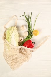 Fresh ripe Chinese cabbage and other vegetables in net bag on white wooden table, top view