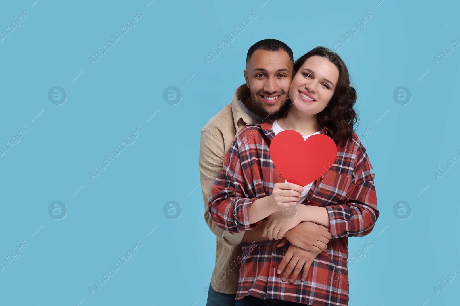 Photo of Lovely couple with red paper heart on light blue background, space for text. Valentine's day celebration