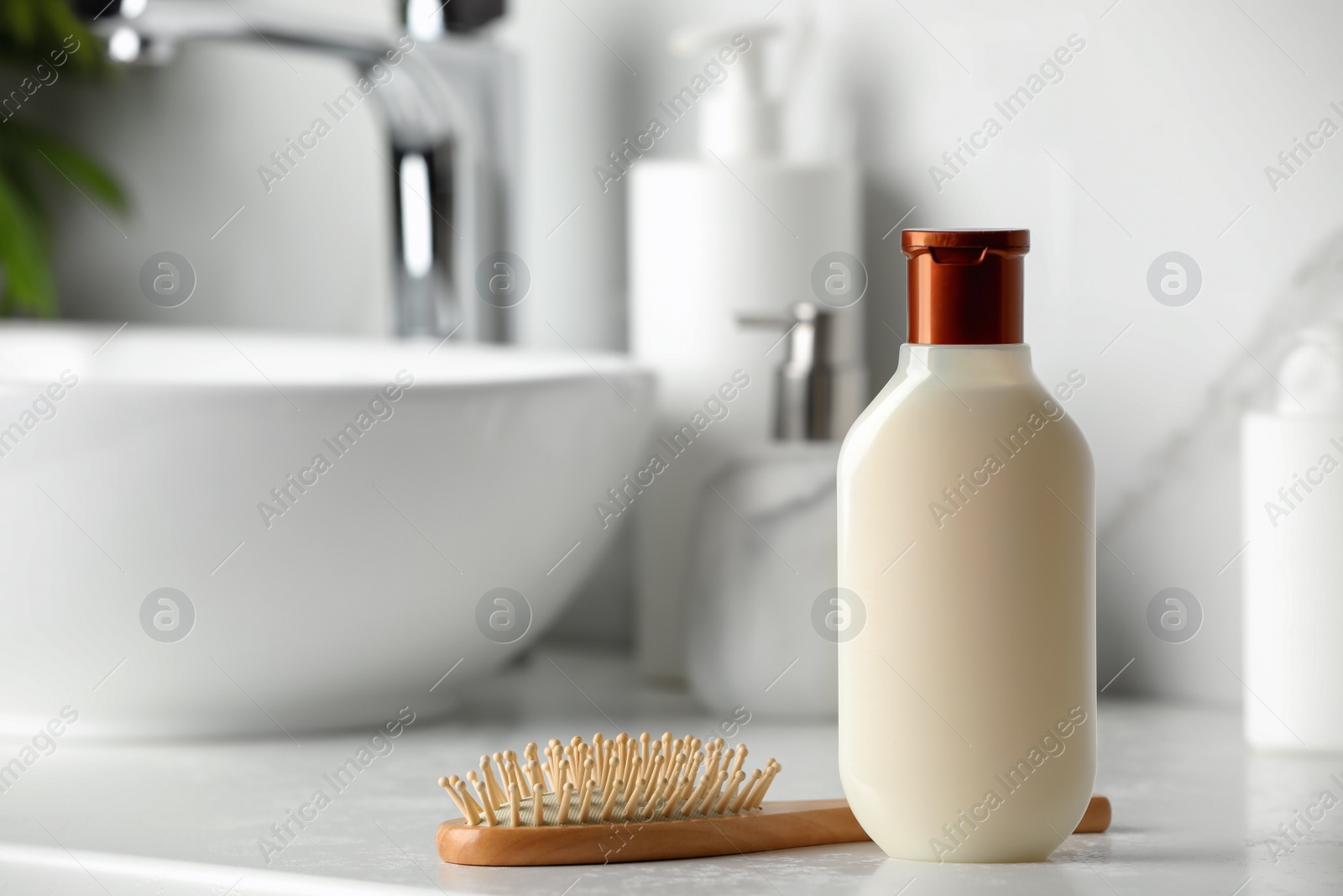 Photo of Bottle of shampoo and wooden hairbrush near sink on bathroom counter, space for text