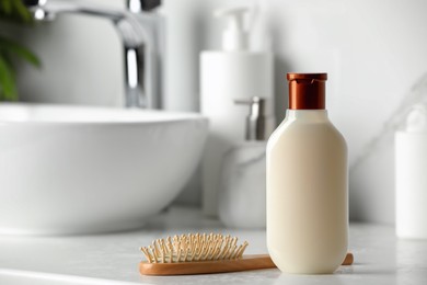 Bottle of shampoo and wooden hairbrush near sink on bathroom counter, space for text