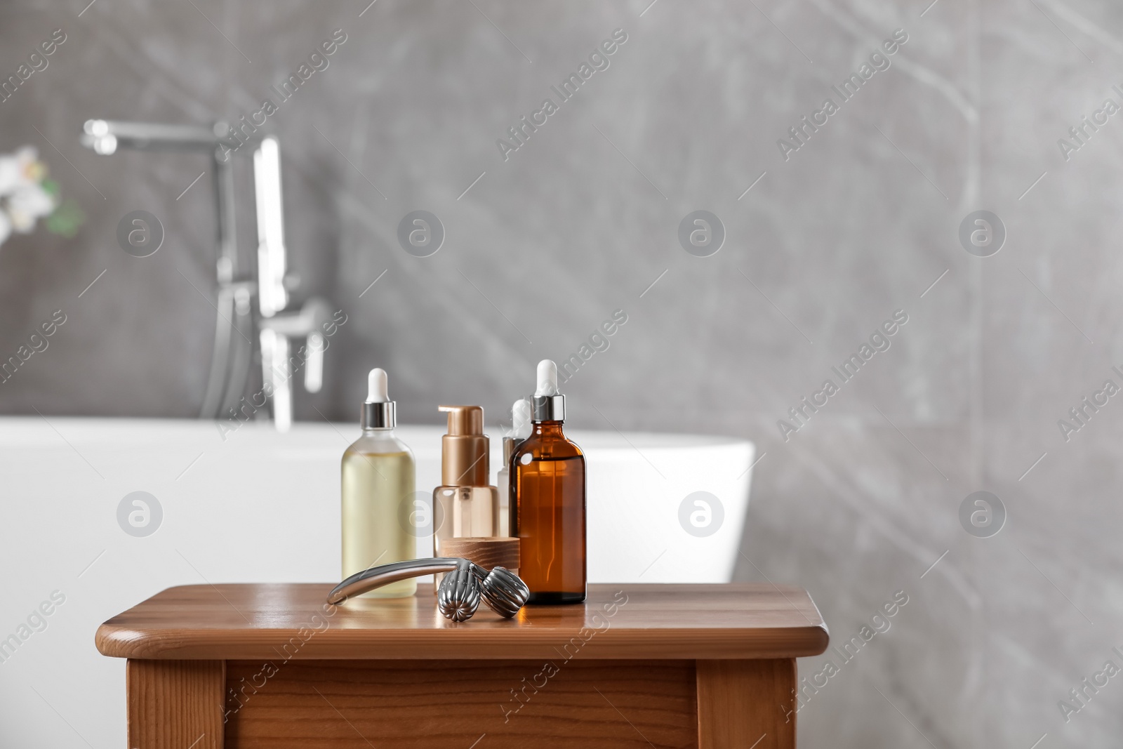 Photo of Metal face roller and cosmetic products on wooden table in bathroom. Space for text