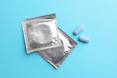 Photo of Pills and condoms on light blue background, flat lay. Potency problem