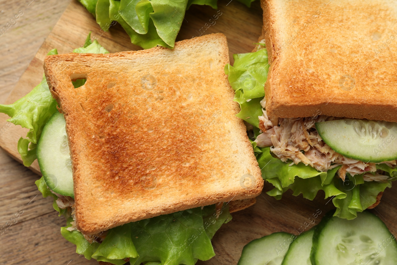 Photo of Delicious sandwiches with tuna, cucumber and lettuce leaves on wooden table, flat lay