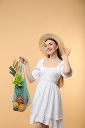 Woman with string bag of fresh vegetables and baguette on beige background, space for text