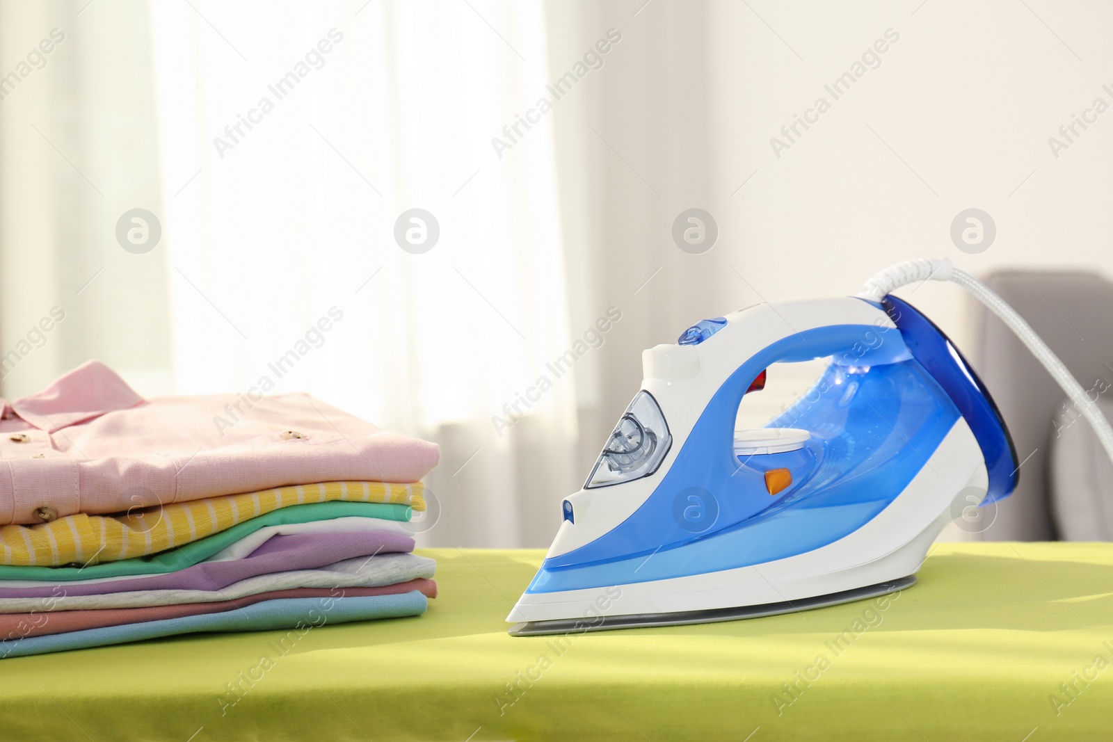 Photo of Board with modern iron and clean laundry at home