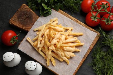 Delicious French fries with cheese sauce, tomatoes, dill and parsley on black table, flat lay