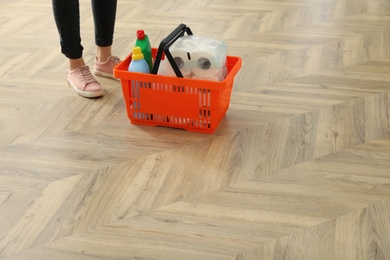 Photo of Woman and shopping basket with household goods on wooden floor, closeup