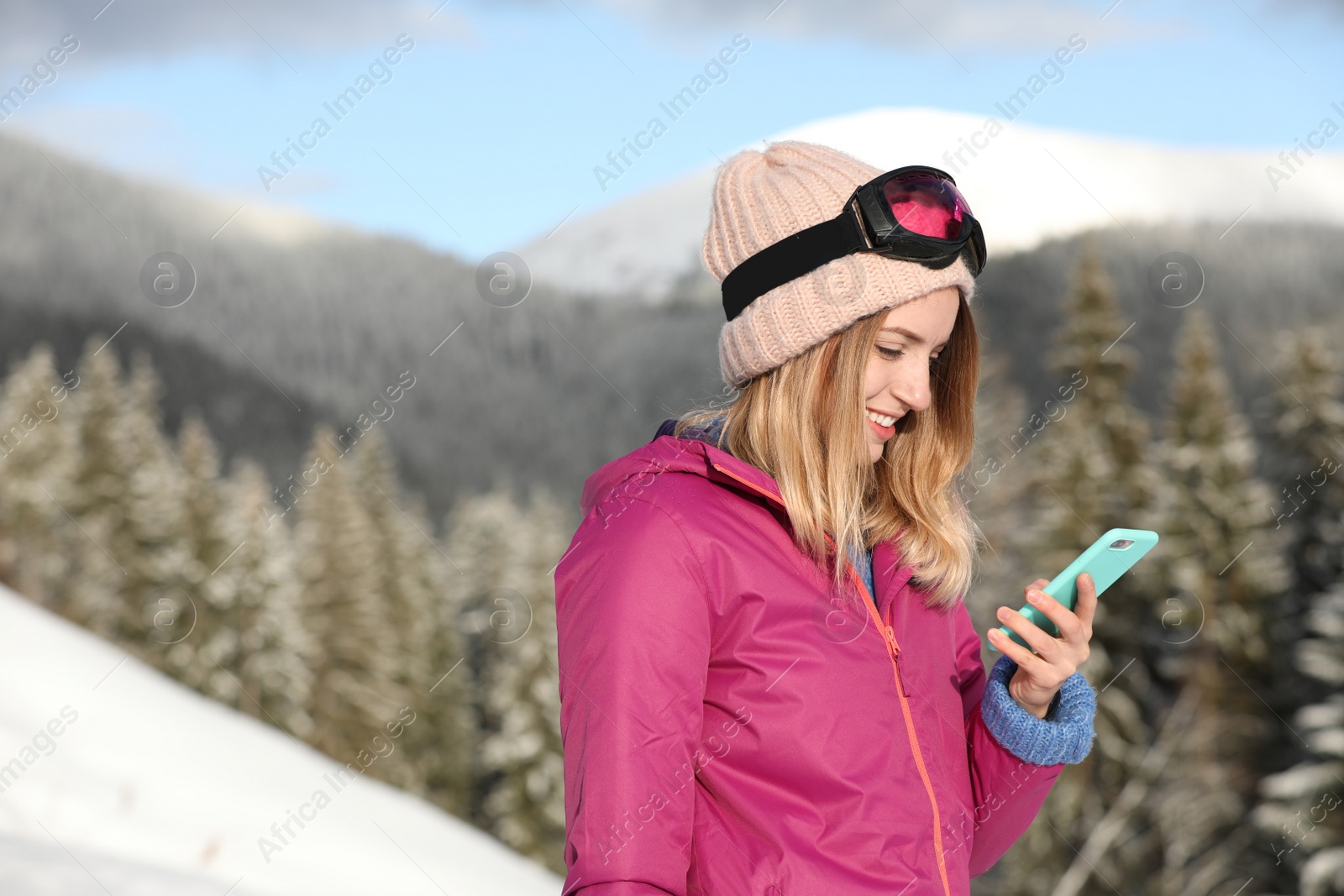 Photo of Young woman with ski goggles using smartphone in mountains during winter vacation