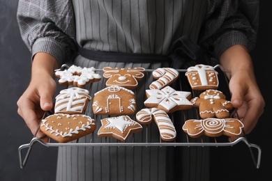 Woman holding cooling rack with delicious homemade Christmas cookies on black background, closeup