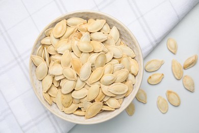 Photo of Bowl with pumpkin seeds on light table, flat lay