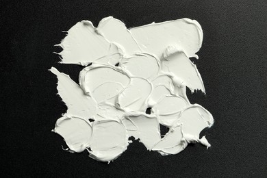 Photo of Strokes of white oil paint on black canvas, top view