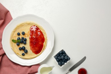 Photo of Stack of delicious crepes with fresh berries and jam on white table, flat lay. Space for text