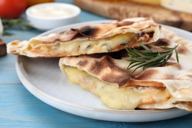 Photo of Tasty pizza calzones with cheese and rosemary on light blue wooden table, closeup