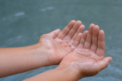 Photo of Kid holding water in hands above sea outdoors, closeup