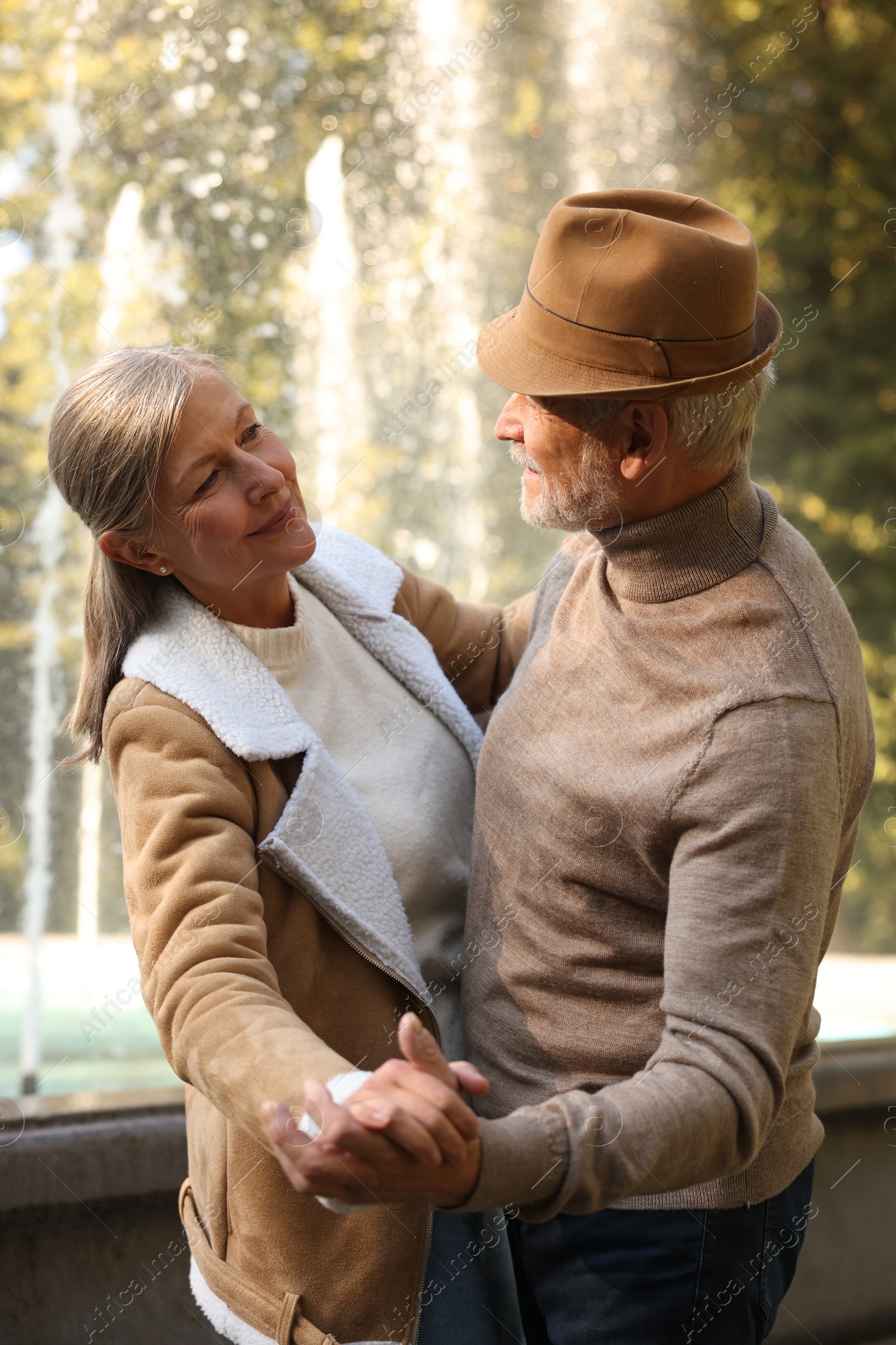 Photo of Affectionate senior couple dancing together near fountain outdoors. Romantic date