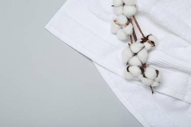 Photo of White terry towel and cotton flowers on light grey background, top view. Space for text
