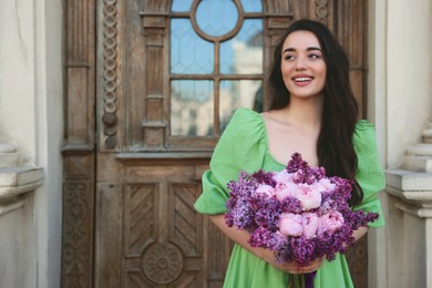 Beautiful woman with bouquet of spring flowers near building outdoors, space for text