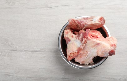 Photo of Feeding bowl with raw meaty bones on white wooden table, top view. Space for text