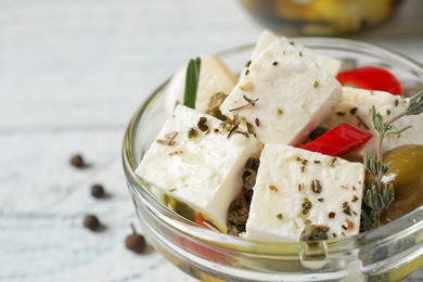 Pickled feta cheese in bowl on white wooden table, closeup