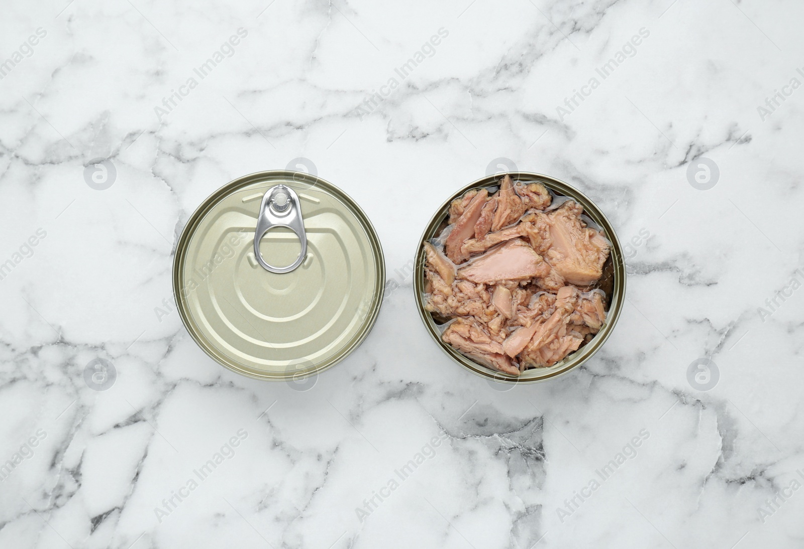 Photo of Tin cans with canned tuna on white marble table, flat lay