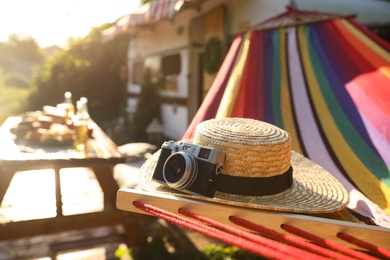 Comfortable hammock with hat and vintage camera near motorhome outdoors on sunny day