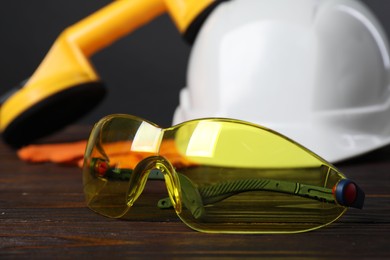 Photo of Goggles, hard hat, suction lifters and protective gloves on wooden surface, closeup