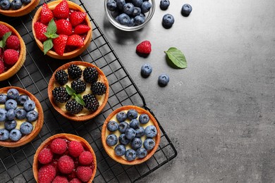 Photo of Tartlets with different fresh berries on grey table, flat lay and space for text. Delicious dessert