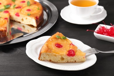 Photo of Piece of delicious pineapple pie with cherry and mint on black wooden table