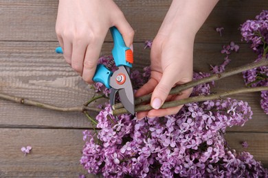Woman trimming lilac branches with secateurs at wooden table, top view