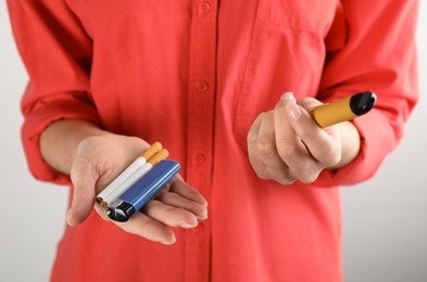 Woman with cigarettes, lighter and vaping device on light background, closeup. Smoking alternative