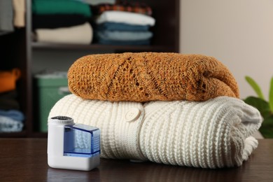 Photo of Fabric shaver and knitted clothes on wooden table indoors