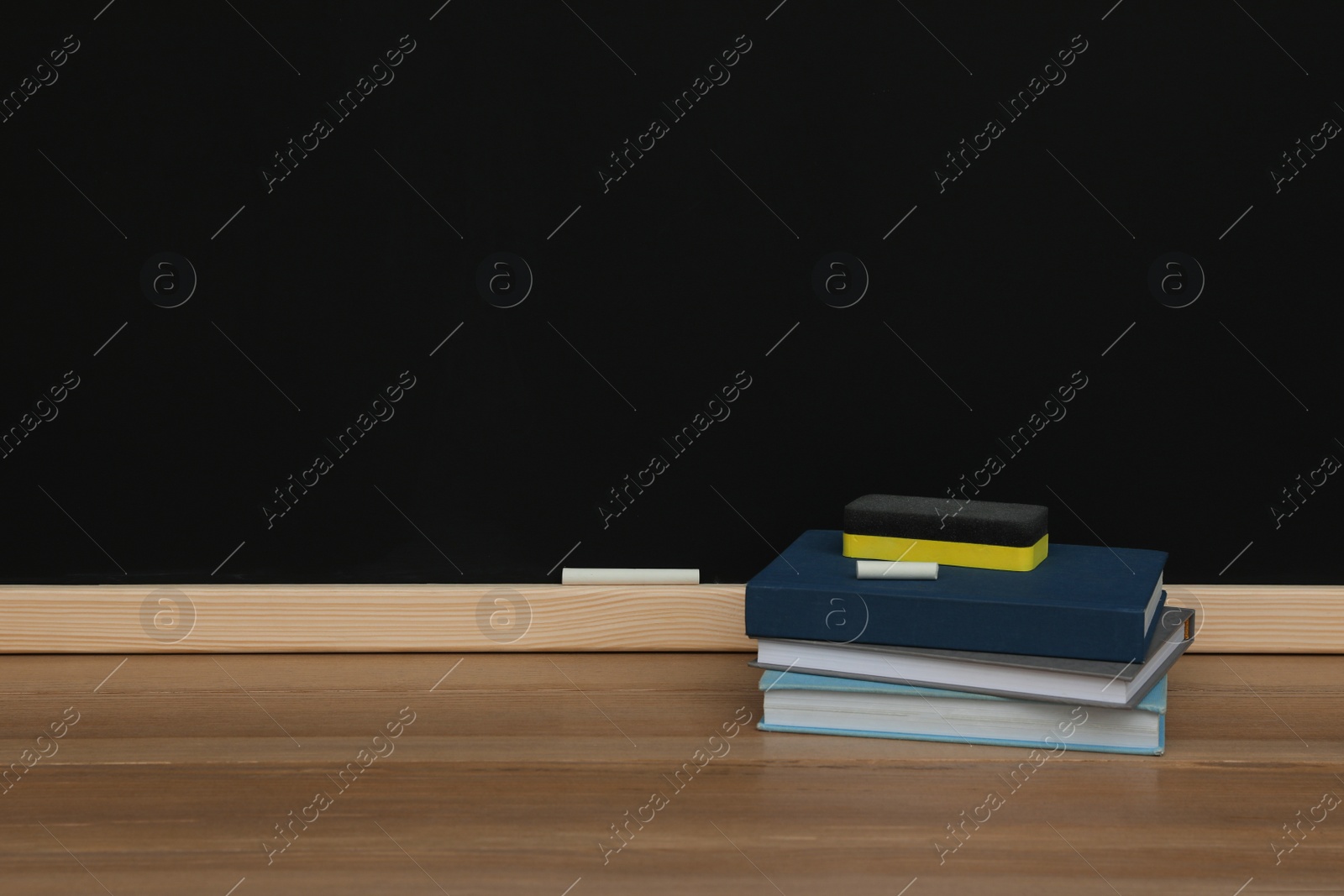 Photo of Books, pieces of chalk and duster on wooden table near blackboard, space for text