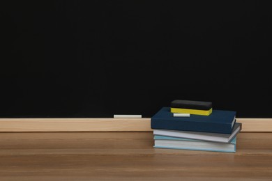 Photo of Books, pieces of chalk and duster on wooden table near blackboard, space for text
