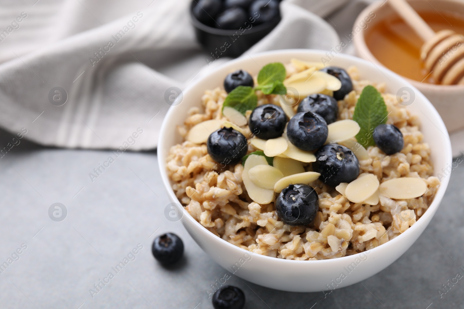 Photo of Tasty oatmeal with blueberries, mint and almond petals in bowl on grey table, closeup. Space for text