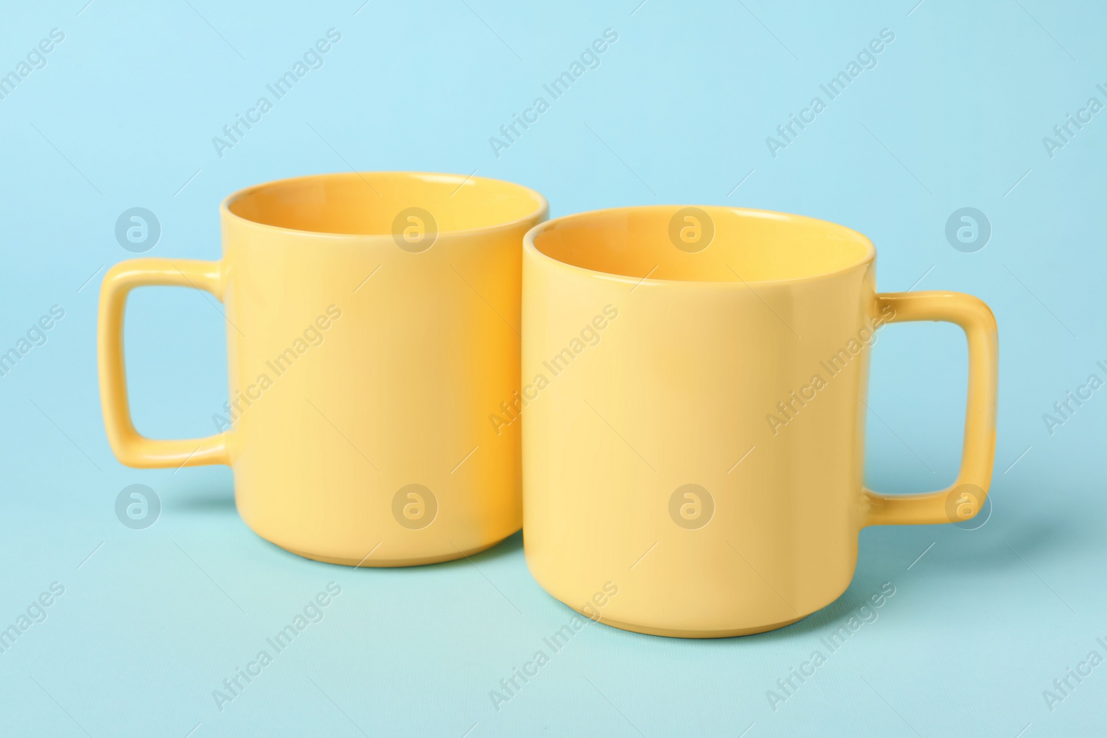 Photo of Two yellow ceramic mugs on light blue background