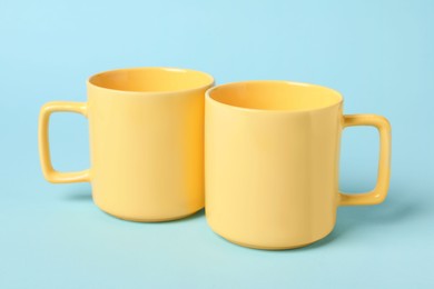 Photo of Two yellow ceramic mugs on light blue background