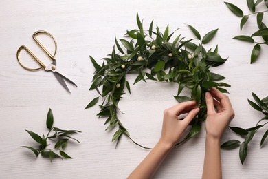 Photo of Woman making mistletoe wreath at white wooden table, top view. Traditional Christmas decor