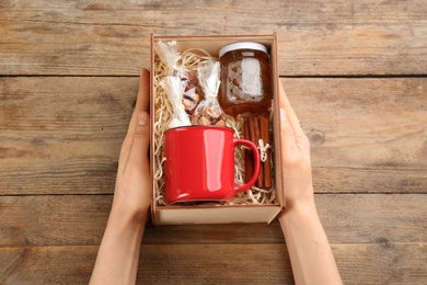 Photo of Woman holding box with stylish craft gift set at wooden table, above view