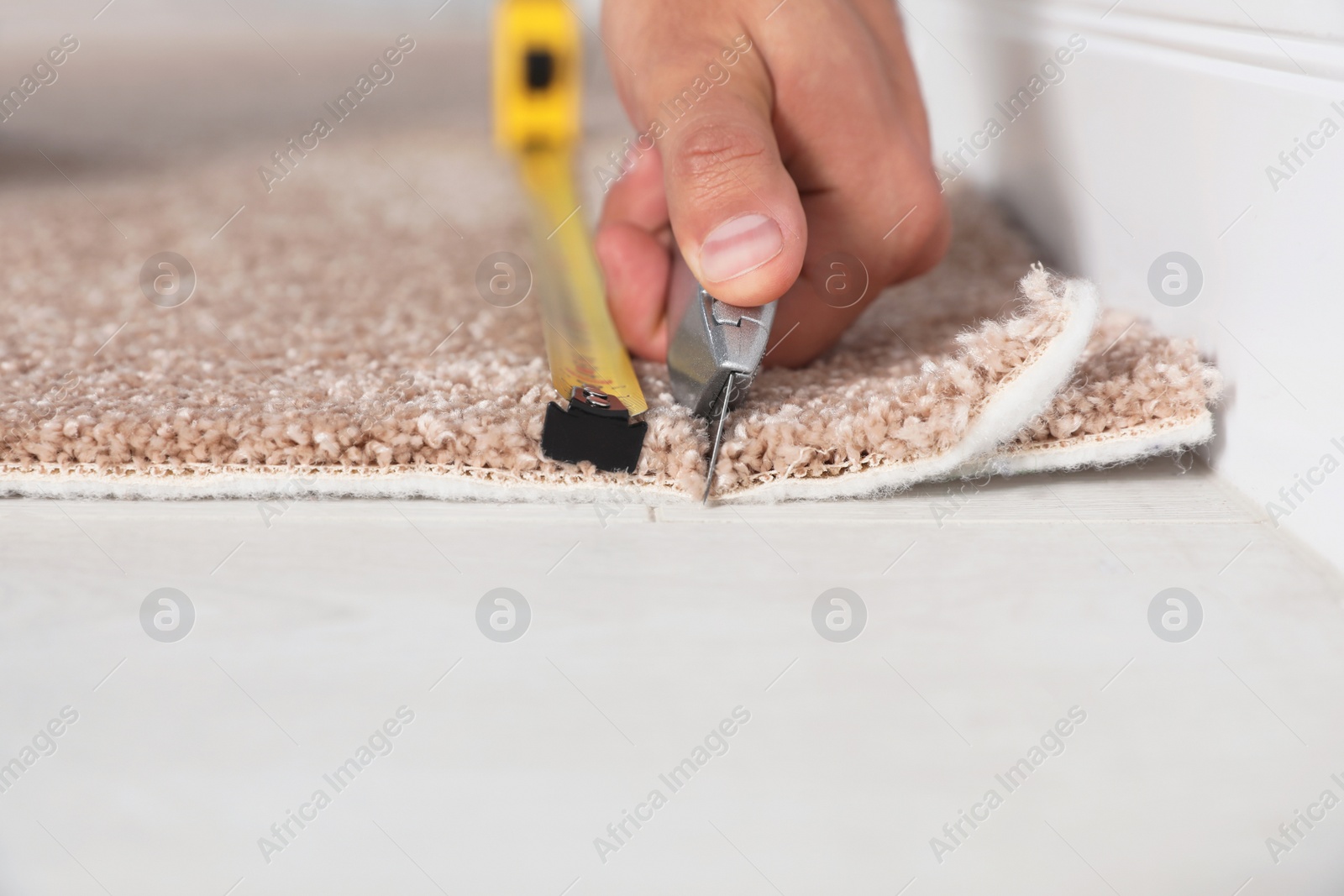 Photo of Man cutting new carpet flooring indoors, closeup. Space for text