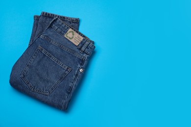 Photo of Jeans with recycling label on light blue background, top view. Space for text