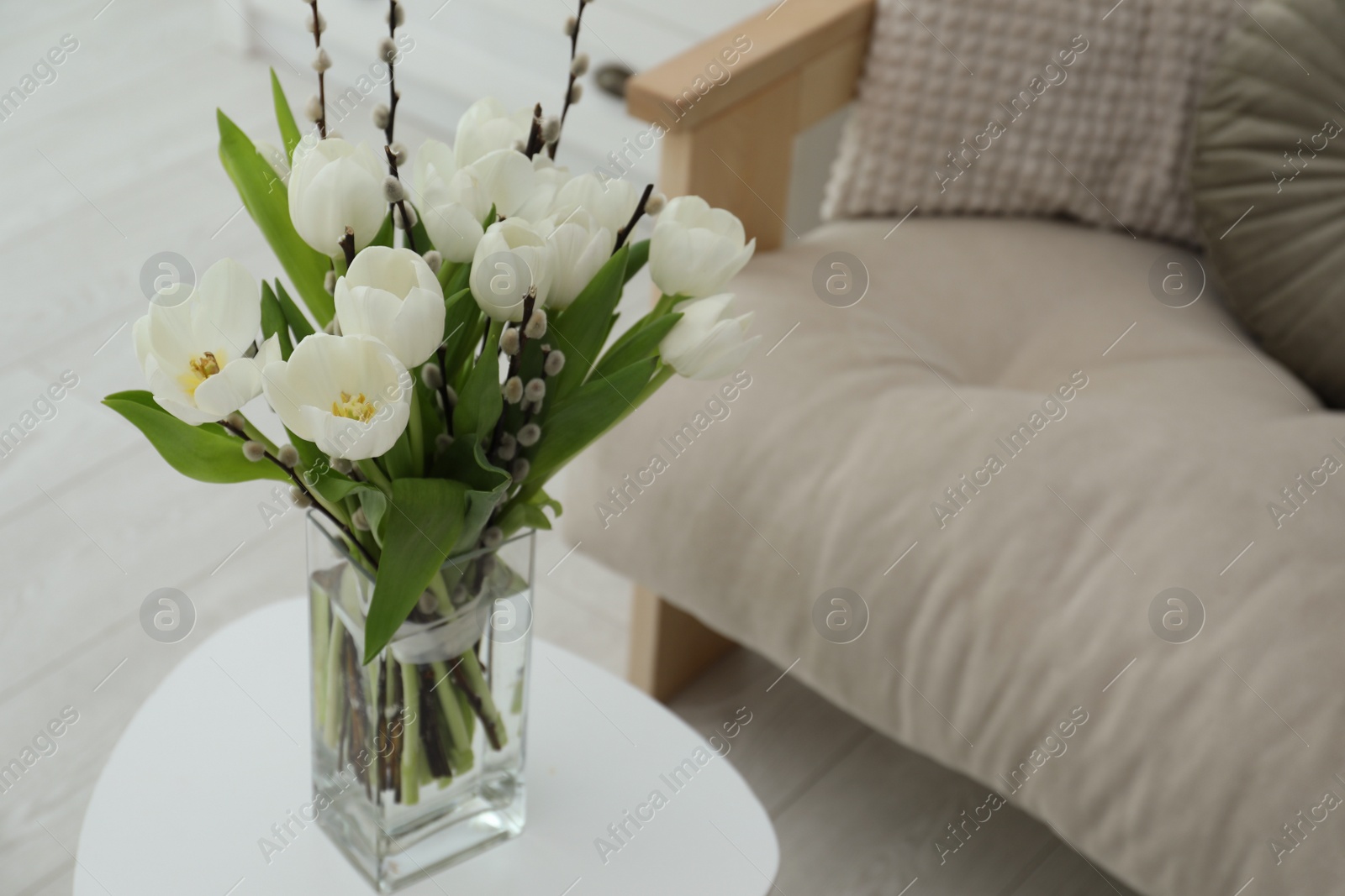 Photo of Beautiful bouquet of willow branches and tulips in vase on table indoors, space for text