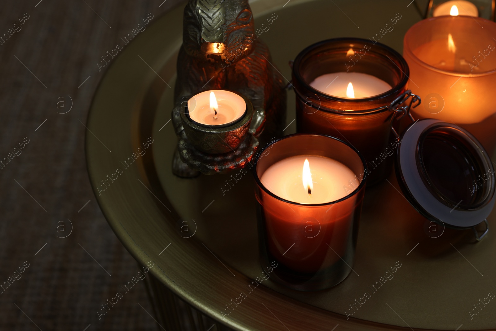 Photo of Burning candles in different holders on table indoors